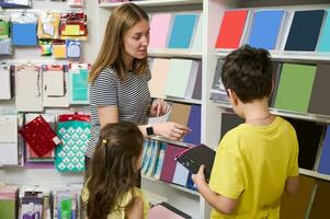 joven mamá, hijo y hija compras para colegio suministros en oficina suministro almacenar, escoger cuadernos para nuevo académico año foto