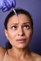 Middle aged woman getting botulinum toxin injection into her forehead area to rejuvenate and reduce signs of ageing and the appearance of the first wrinkles on her face. Injection cosmetology concept photo
