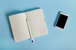 Flat lay of a smartphone and a white pencil on an opened daily, lying on blue background with copy space for text photo