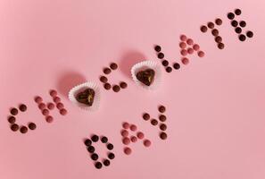 CHOCOLATE DAY lettering laid out from multi colored chocolate pills and pralines on pink background with copy space photo