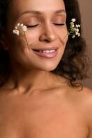 Serene delighted pretty natural beauty young woman with closed eyes and beautiful toothy smile posing with Gypsophila sprigs on her face. Skin care and body positivity concept. Cosmetology dermatology photo