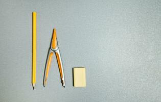 Pencil, eraser and compass. Flat lay composition of yellow office tools on a gray background. photo