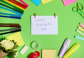 Top view of colorful assortment of stationery office supplies and school accessories arranged in a circle, with white paper in the center with lettering Happy Teacher's Day photo