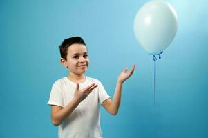 hermoso chico señalando en azul globo y linda sonrisas mirando a cámara. azul antecedentes con Copiar espacio foto