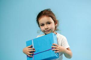 Adorable girl with blue gift on blue background with copy space. Children Day. Birthday concept. photo