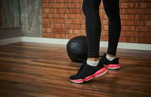 Close-up of female legs in sport shoes next to a medicine ball on the floor against a red bricks wall background with copy space photo