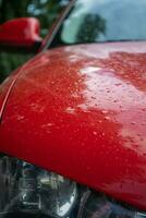 detalle de un rojo coche con gotas de lluvia en el capucha. foto