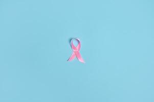 Flat lay of a satin pink ribbon awareness, International symbol of Breast Cancer Awareness Month in October. Isolated over on blue background with copy space . Medical and Women's health care concept. photo