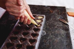 Closeup of squeezing filling of salted caramel cream from confectionery bag into candy molds for preparing chocolate pralines photo