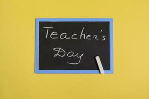 Flat lay of a blackboard with inscription Teachers Day on a yellow background with space for text photo