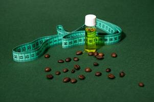 Still life transparent bottle of massage anti-cellulite oil, measure tape and coffee beans scattered on green background photo