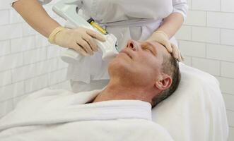 Beautician doing facial mesotherapy treatment on relaxed mature handsome Caucasian man in modern wellness spa center. Man getting face tightening injections at cosmetology clinic. photo