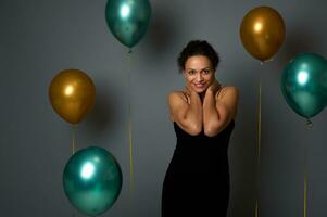 retrato de contento bonito mujer en noche negro vestir sonriente con hermosa con dientes sonrisa posando en contra aire globos en gris pared antecedentes con Copiar espacio para Navidad, nuevo año, aniversario anuncio foto