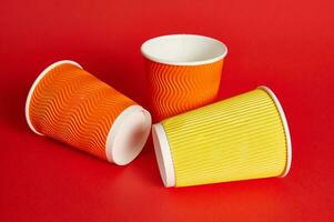 Multi-colored paper cups for a hot drink lying on a red background with copy space. Shot with soft shadow. Recyclable cardboard mugs. photo