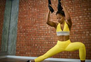 Attractive woman doing glute exercises, performing side lunges while working out with suspension straps in fitness studio. Fitness, stretching, active lifestyle concept photo