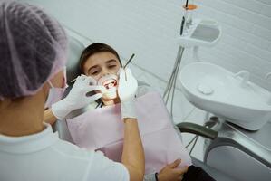 Close-up of elementary aged boy with opened mouth and cheek retractor at dental appointment in contemporary modern dental clinic. Overhead view of paediatrician dentist treating child's teeth photo