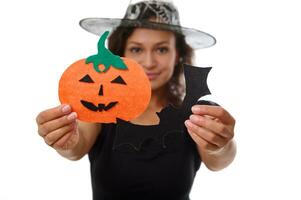 Focus on cut felt handmade pumpkin and bad in the hands of a blurred beautiful woman dressed in witch carnival costume isolated on a white background with copy space for Halloween advertisement photo