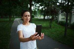 Woman using mobile phone, takes photo, browsing news feed, shares content on social media while walking along park alley photo