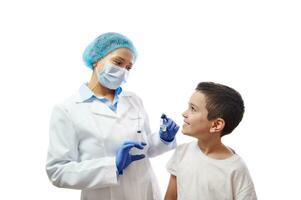 Little boy looking at a smiling doctor in medical mask with vaccine vial and syringe on hands. Copy space photo