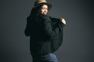 Fashionable curly Latina woman in straw hat and stylish blazer, looking through her shoulders, posing back to camera photo