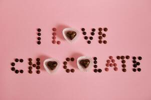 Flat lay of I LOVE CHOCOLATE lettering laid out from multi colored chocolate pills and pralines on pink background with copy space photo