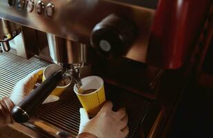 Coffee machine pourig coffee to yellow cardboard coffee cup in bar. Cropped image. Closeup photo