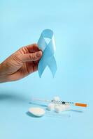 Close-up of hand holding blue ribbon, symbol of World Diabetes Awareness Day on blue background with insulin syringe and pure refined white sugar cubes. Concept of dangers of eating white sugar photo