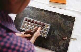 Chocolatier squeezing liquid warm chocolate mass from confectionery bag into candy molds. photo