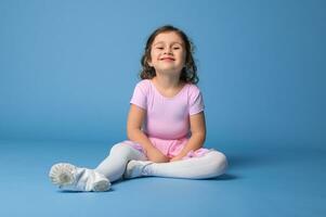 Beautiful and funny little girl in pink dress posing to camera while relaxing on blue background with space for text photo