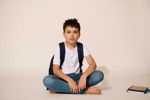 Handsome teenager, primary school student sitting against a white studio background, looking confidently at camera. photo