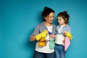 Cute mother gently hugs her little daughter and smiles while posing on a blue background with detergents in hands photo