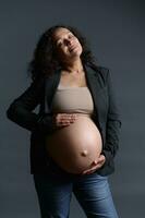 grávido mujer, expectante madre golpes su embarazada barriga terminado gris antecedentes. 40 semana de contento despreocupado el embarazo. foto