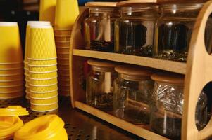 Closeup of yellow cardboard cups inverted on a coffee machine and transparent glasses containers with tea photo