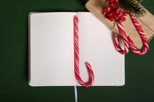 Christmas concepts. Beautiful simple present in craft wrapping gift paper with holly and candy canes on it, sugary striped lollipop on the middle of the notepad with blank empty pages with copy space photo