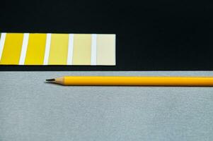 Designer colored swatches and wooden pencil on black background. Gradient of yellow on color wheel. photo