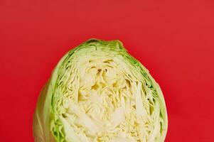 Cropped image of a half cut young green cabbage on a red background with copy space. Color contrast. photo