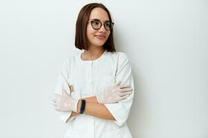 Happy young doctor intern looking away while posing against white background with crossed arms photo