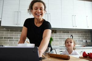 Mother and daughter watching recipe of meal, standing on a kitchen. Mother and daughter prepare dough together. Love, affection, tenderness, femily relationships. photo