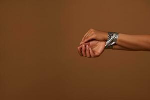 Cropped view of female hands tied with duct tape against a dark beige background. Social concept for International Day to End Aggression, Inequality and eliminating violence against Women. Copy space photo