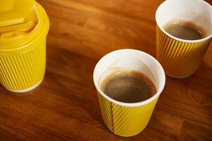 Yellow coffee cardboard cup on wooden background. Yellow takeaway paper cups with hot coffee on a wooden surface photo