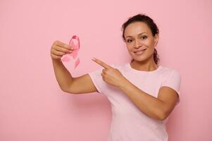 Hispanic woman holding a pink ribbon, symbol of World Breast Cancer awareness Day, in 1 st October. Woman's health care concept, October Pink day, World Cancer Day, national Cancer Survivor Day. photo