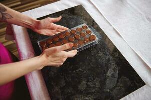 Close-up of female hands holding chocolate molds full of liquid heated chocolate mass photo