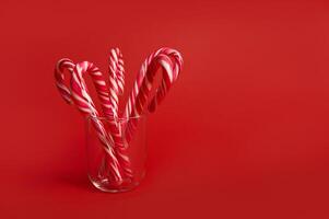 Beautiful minimalis simple composition with lollipops on transparent glass on bright red background with copy space for christmas ad photo