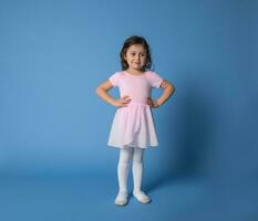 linda niña bailarina vestido en rosado uniforme posando dentro el cámara con brazos en cintura foto