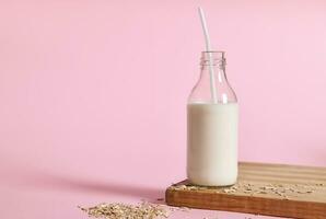 Vegan oat milk on wooden board and oatmeal scattered on pink background photo