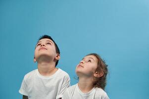 A boy and a girl in white T-shirts sit on a blue background next to each other and look up photo