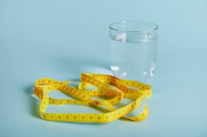 A glass with water and a measuring tape isolated on blue background with space for text photo