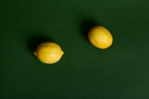 plano laico composición de dos brillante amarillo limones en un oscuro verde antecedentes , estudio Disparo con suave ligero. comida antecedentes. vegano sano comiendo. Copiar espacio para anuncio foto