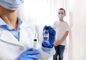 Vial with vaccine and syringe in the hands of pediatrician on the blurred background of a little boy photo