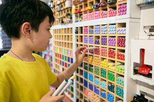 adorable adolescente chico toma fuera acuarela marcadores desde un estante mientras comprando dibujo y dibujar herramientas en papelería Tienda foto